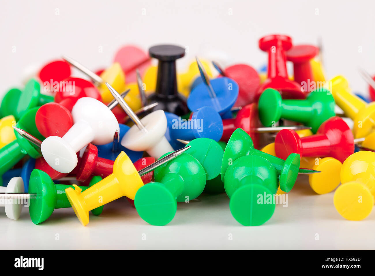 Pile of colorful pushpins on a white surface. Pile of thumbtacks isolated on white background. Stock Photo
