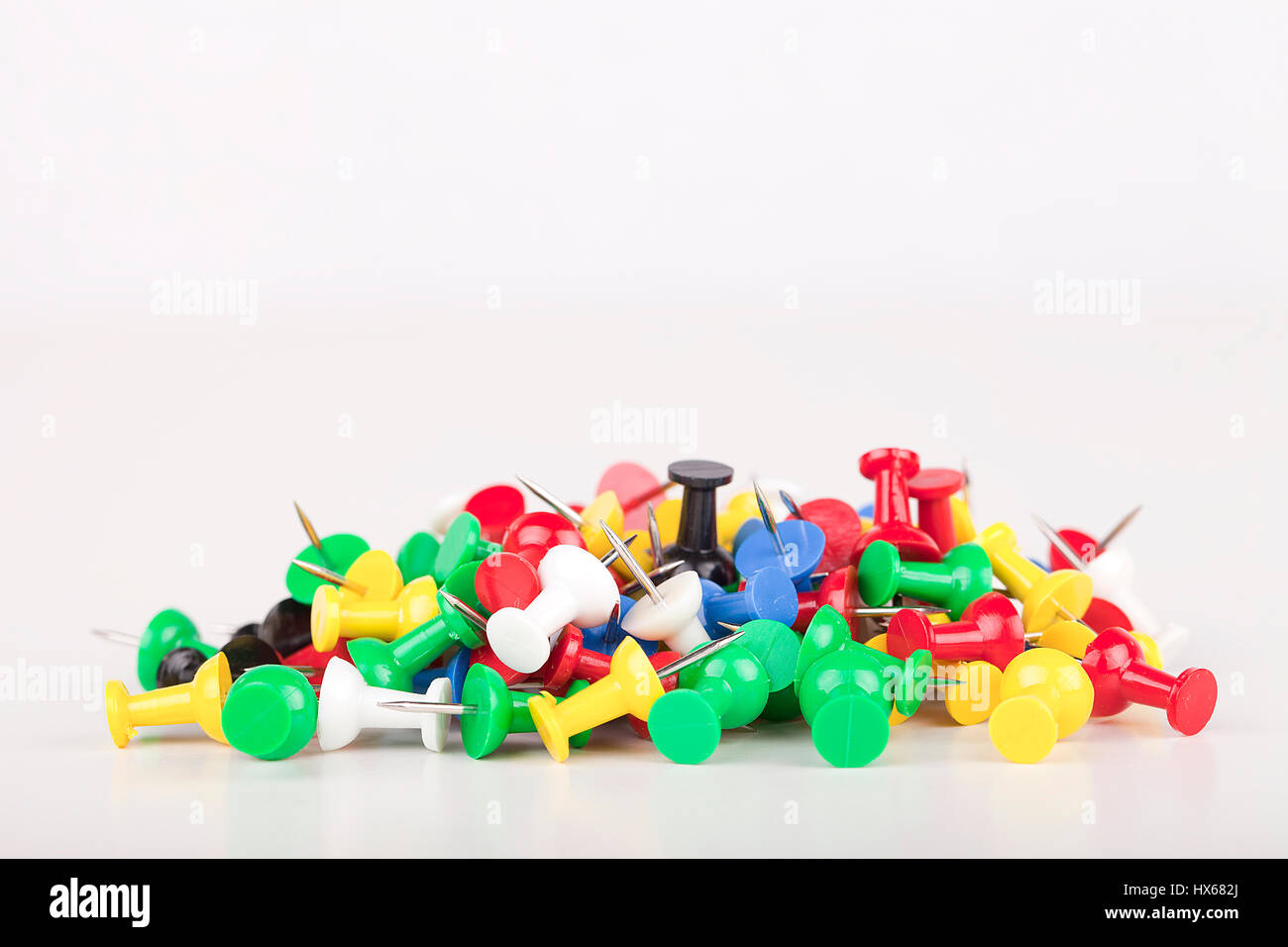 Pile of colorful pushpins on a white surface. Pile of thumbtacks isolated on white background. Stock Photo