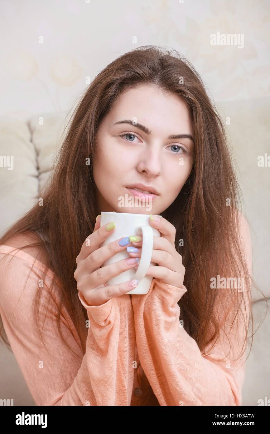 Happy young woman sitting on sofa in cosy cloths with cup of coffee Stock Photo