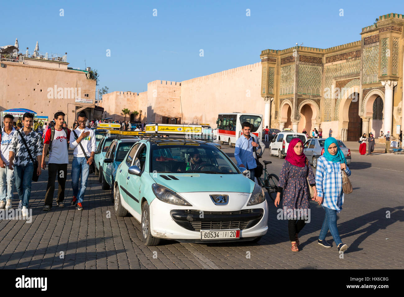 Meknes, Morocco.  Petit Taxis in front of the Bab Mansour.  Young Moroccan Men and Women. Stock Photo