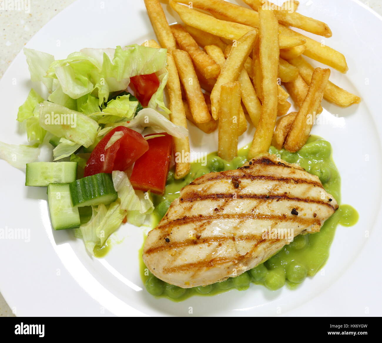 Grilled chicken breast on a bed of green pea puree and peas, served with a salad and french fried potato chips, top view Stock Photo