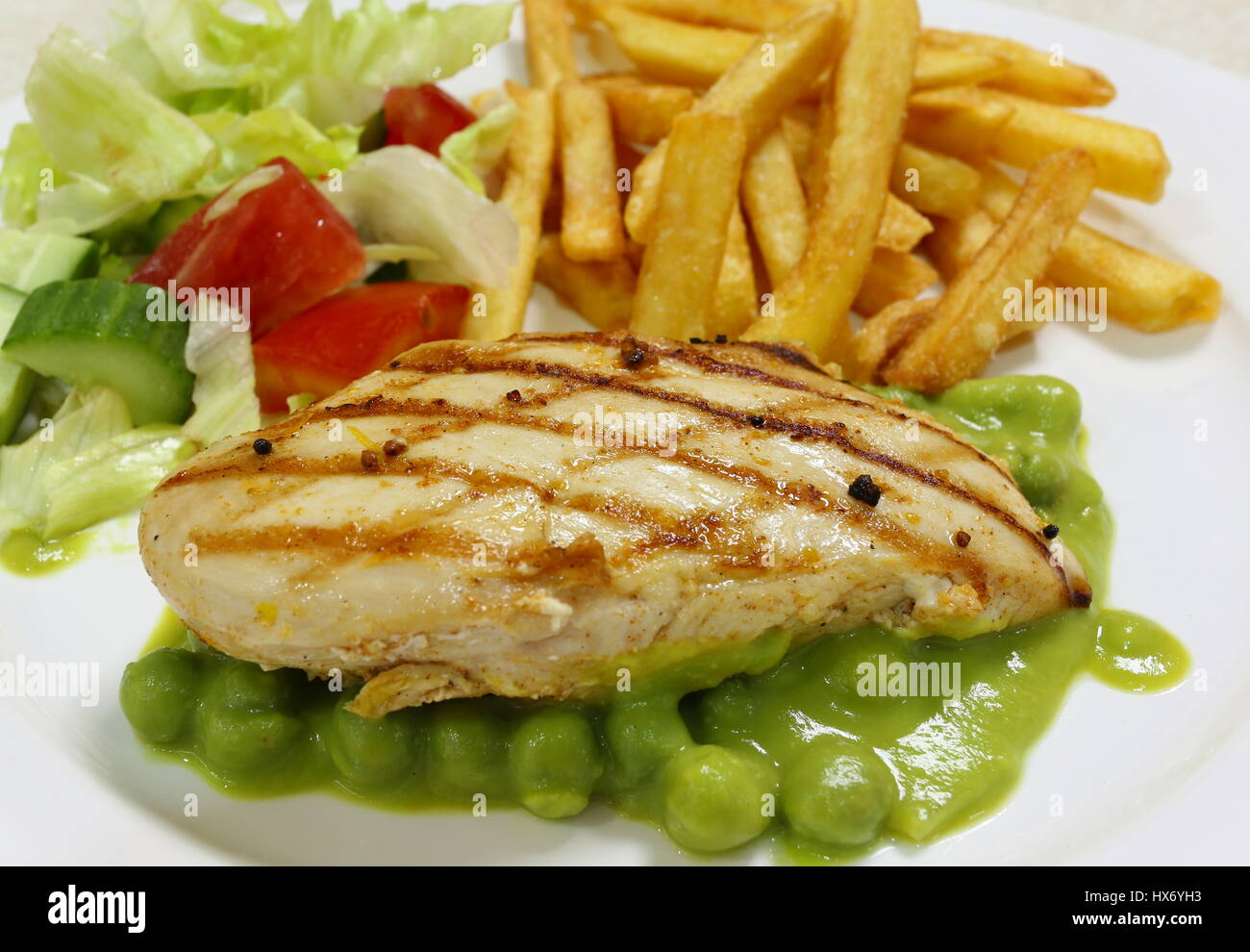 Grilled chicken breast on a bed of green pea puree and peas, served with a salad and french fried potato chips, side view Stock Photo