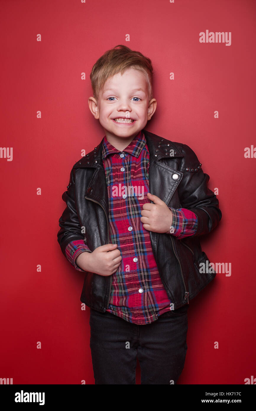 Fashion little boy wearing a leather jacket. Studio portrait over red