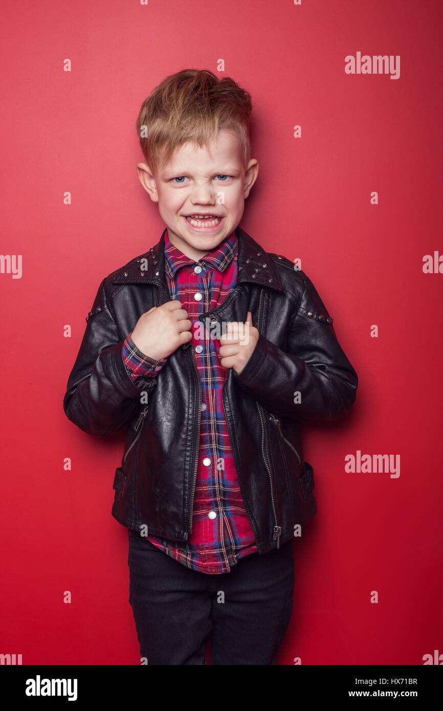 Fashion little boy wearing a leather jacket. Studio portrait over red background Stock Photo