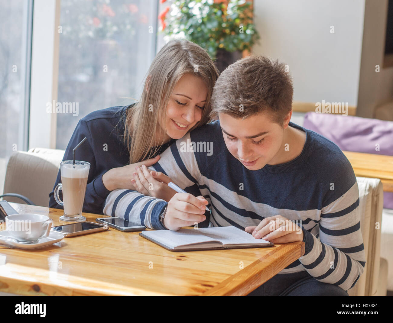 Beautiful young couple  sitting in cozy coffee shop. Couple in love making planning of life and writing in notepad. Stock Photo
