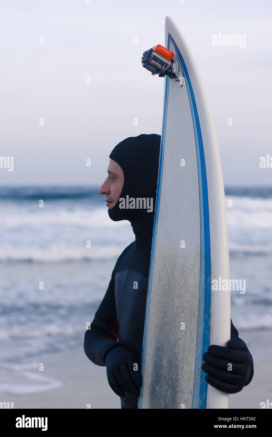 Wet surfer with surfboard standing on the sand on the beach Stock Photo