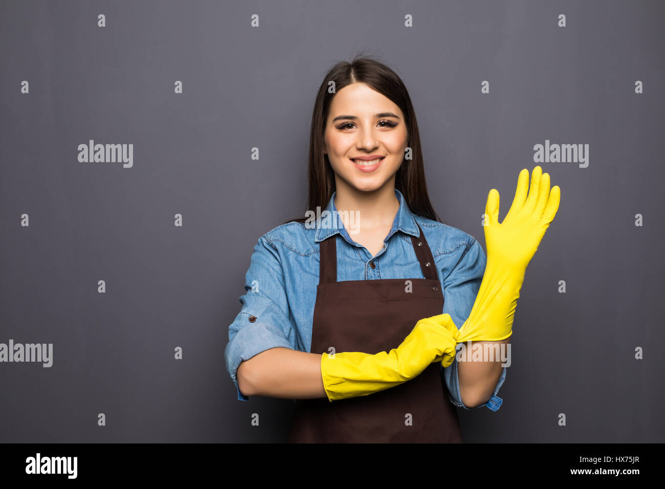Cheerful housewife putting on gloves before cleaning on grey Stock Photo