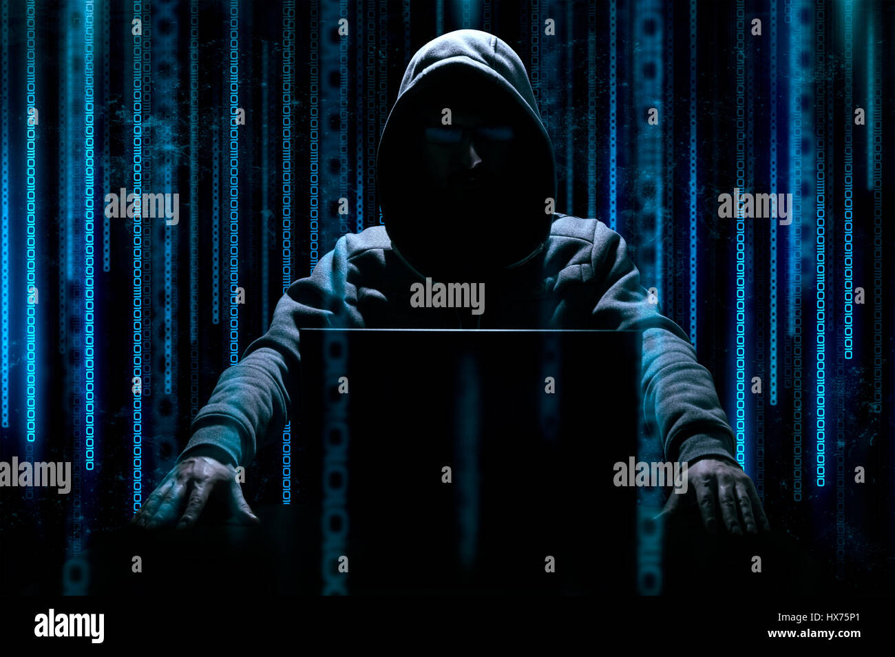 Hacker sits behind laptop with binary code on background Stock Photo