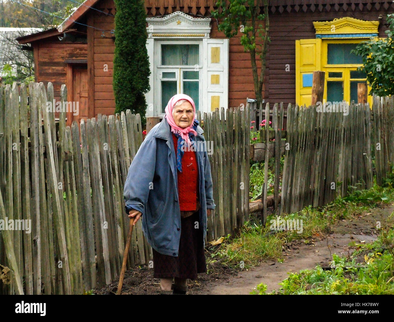 An old woman a babushka leans on her cane in the garden of a