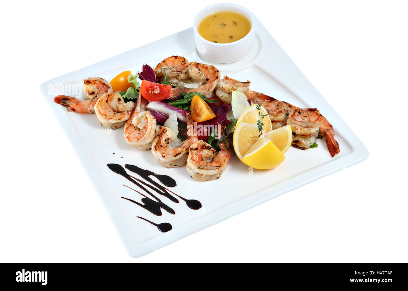 Shrimp grilled with vegetables, lemon and sauce on white square serving platter, isolated on white background. Stock Photo