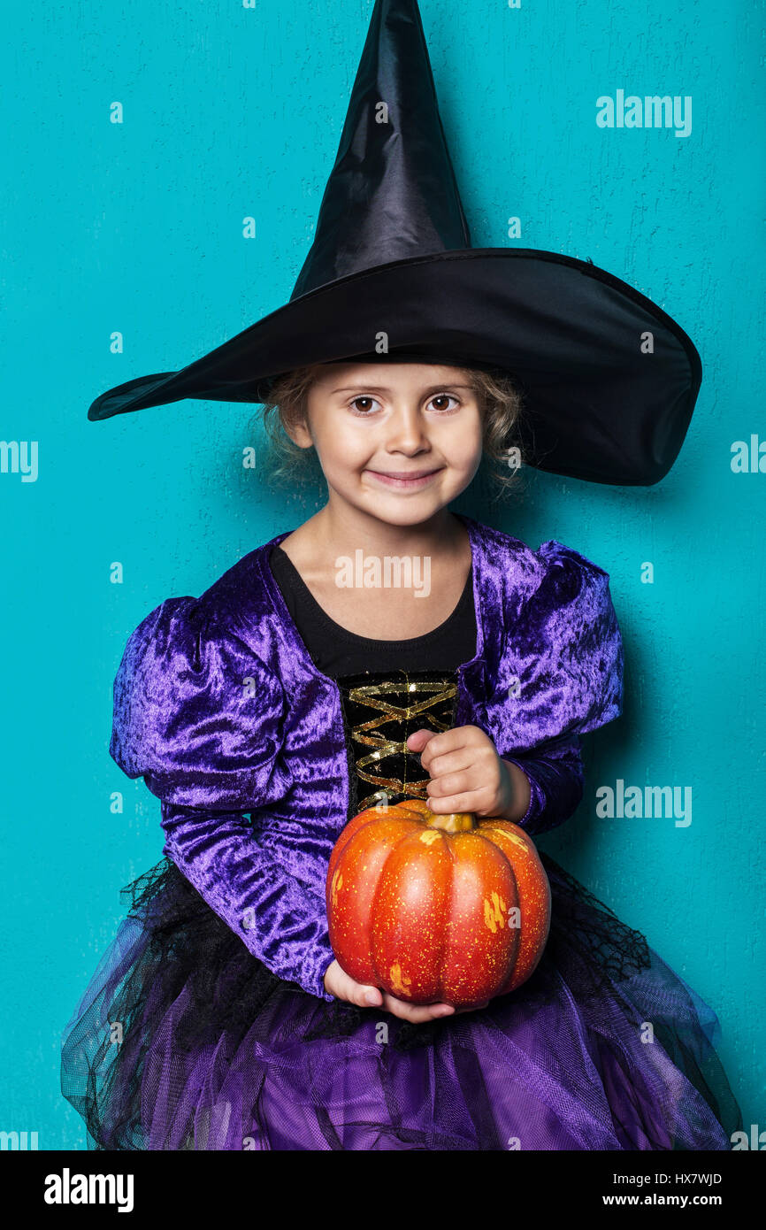 Portrait of little girl in black hat and witch clothing with pumpkin ...