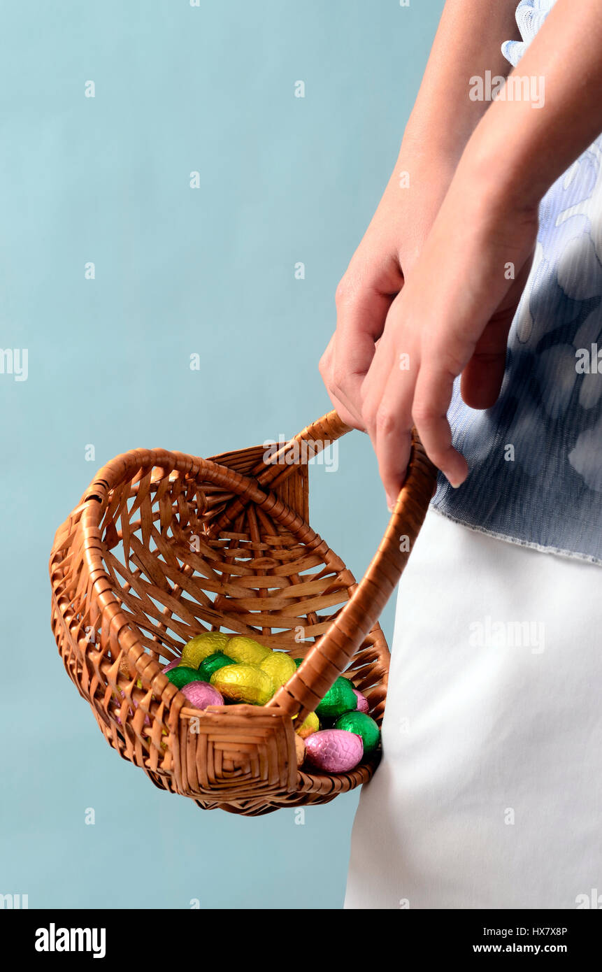 Child's hand holding easter egg basket and blue and white dress Stock Photo