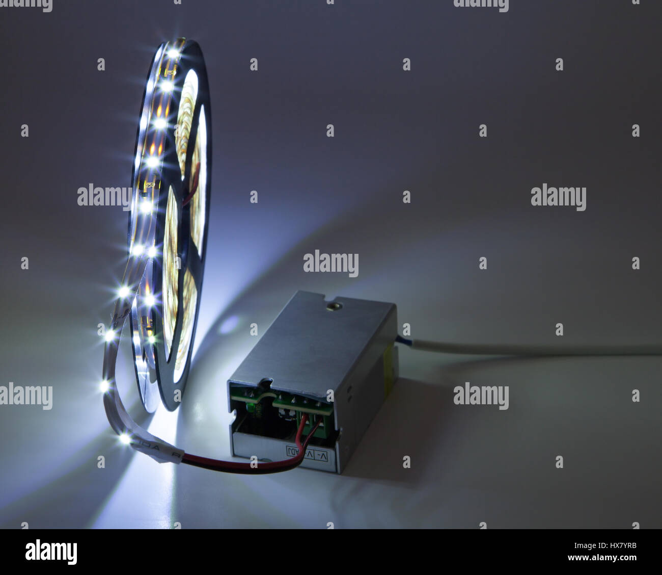 Coil of luminous LED strip light connected to voltage transformer. Stock Photo