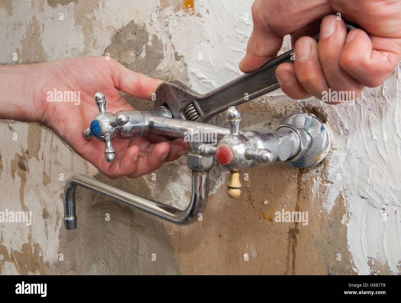 Fix a leaking tap, close-up of hands plumbing unscrew connecting nut wall faucet using an adjustable wrench. Stock Photo