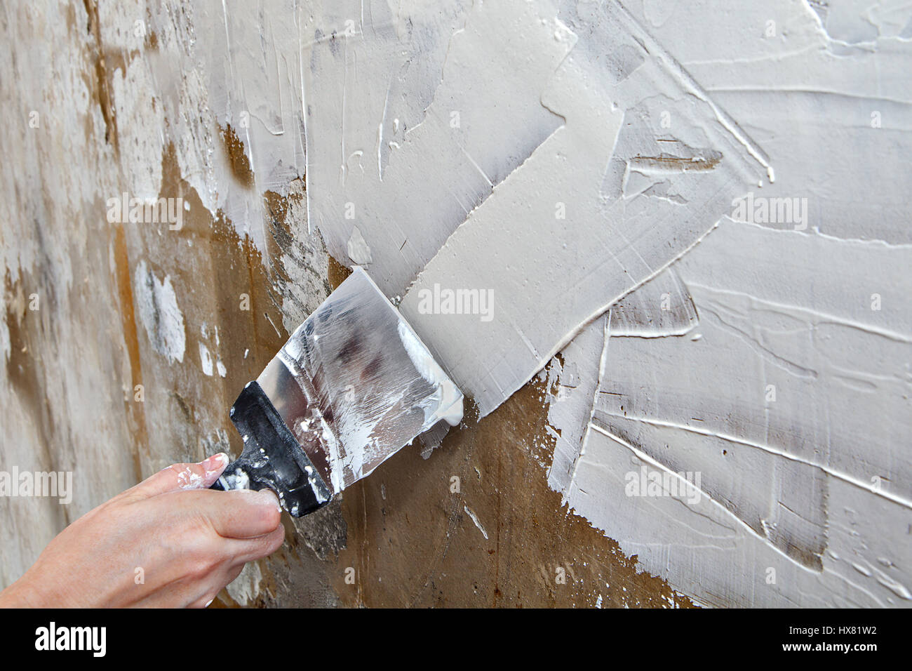 Align the wall with a painting ground coat, painter hands holding spatula, close-up. Stock Photo
