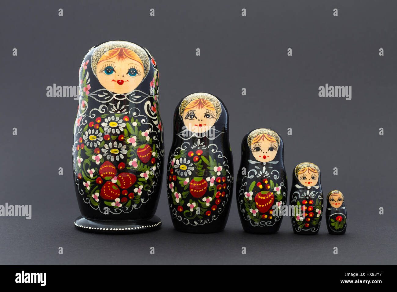 Beautiful black russian nesting dolls (matryoshka dolls) with white, green and red painting in front of dark background Stock Photo