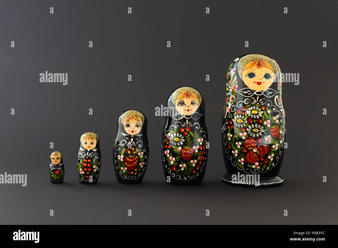 Beautiful black russian nesting dolls (matryoshka dolls) with white, green and red painting in front of dark background Stock Photo