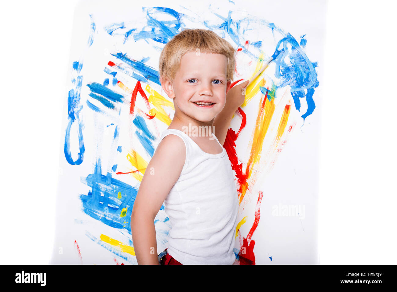 Little messy kid painting with paintbrush picture on easel. Education. Creativity. School. Preschool. Studio portrait over white background Stock Photo