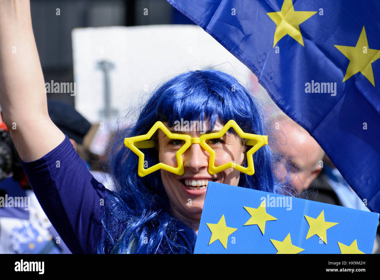 London, UK. 25th Mar 2017. Portrait of a smiling anti-Brexit protester wearing yellow EU stars as glasses, blue wig and waving European Union flag at the Unite for Europe march in London. Thousands of protesters marched through central London protesting against Brexit during the 60th EU anniversary, just before the Theresa May triggered Article 50. Credit: ZEN - Zaneta Razaite/Alamy Live News Stock Photo