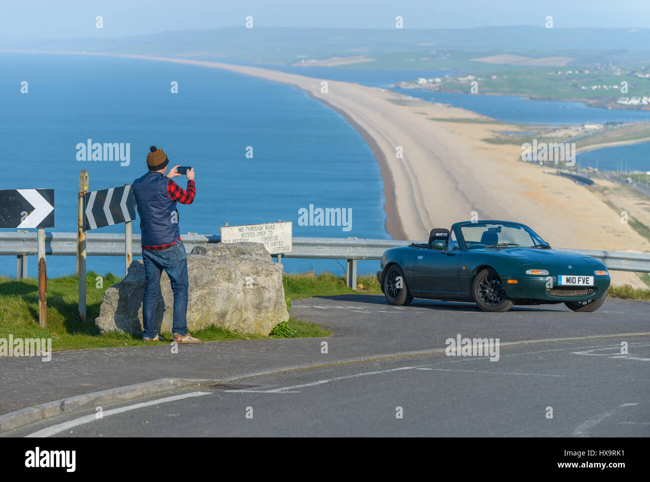 Portland Harbour, Dorset, UK. 26th March 2017. A man takes a picture of a car with his phone high above Chesil Beach on a crisp windy sunny day at Portland Harbour on Mothering Sunday.  © Dan Tucker/Alamy Live News Stock Photo