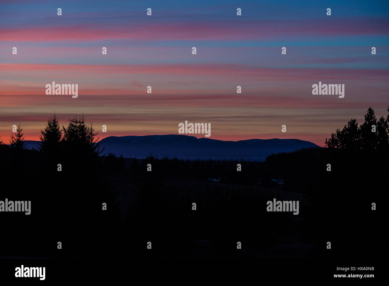 The sun sets behind Ben Wyvis in the Scottish Highlands, near Inverness on the first day of British Summer Time & another day of glorious sunshine and clear blue skies in the Highlands. Stock Photo