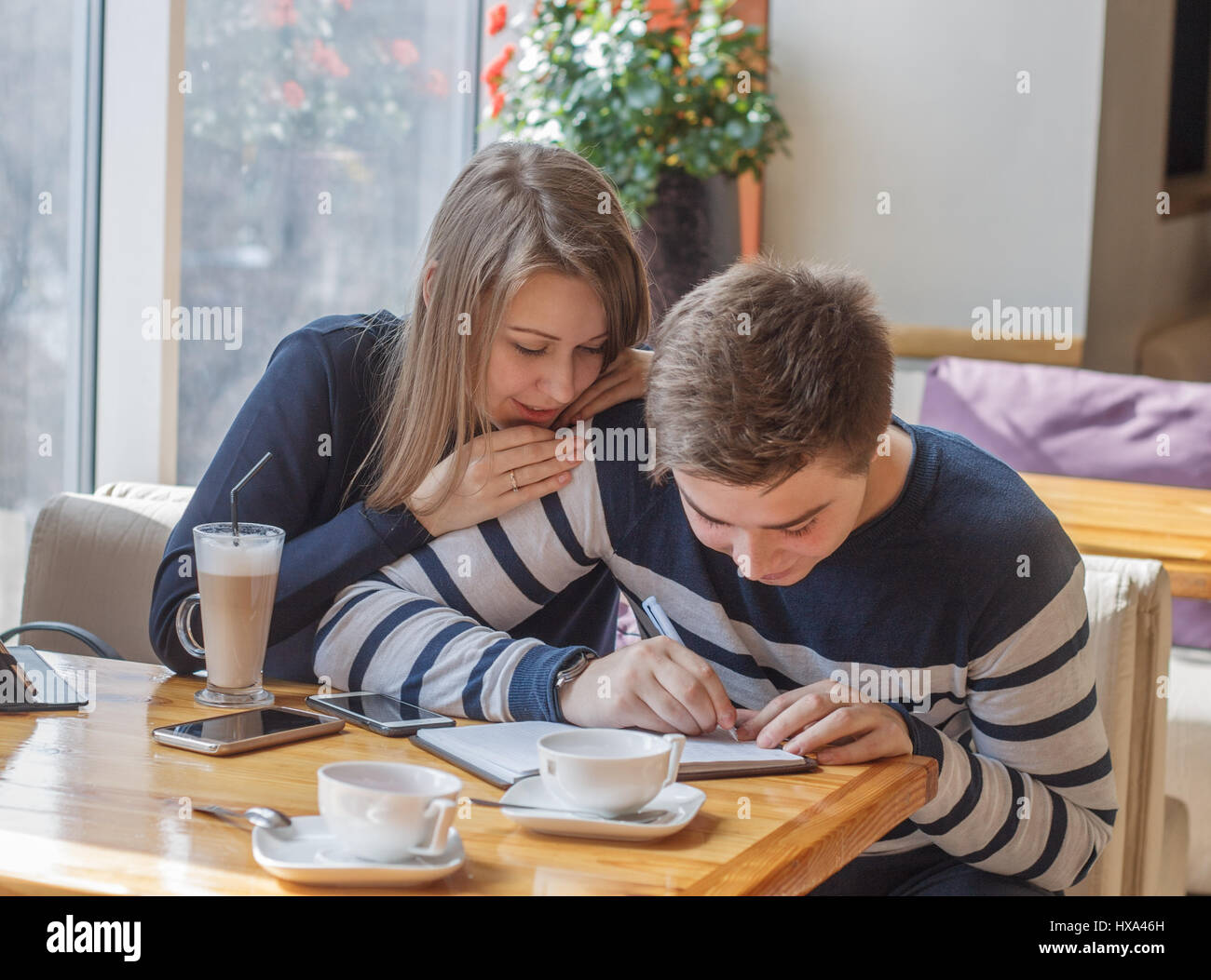 Beautiful young couple sitting in cozy coffee shop. Couple in love making planning of life and writing in notepad. Stock Photo
