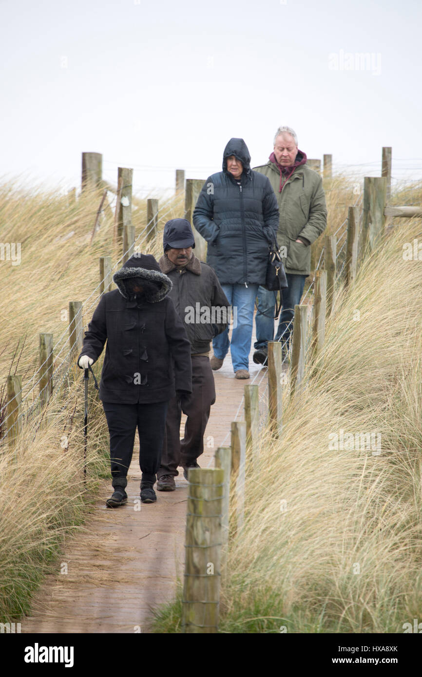 Wet and windy weather as beach visitors brave the elements walking along a path through the sand dunes at Talacre Beach in Flintshire, North Wales Stock Photo