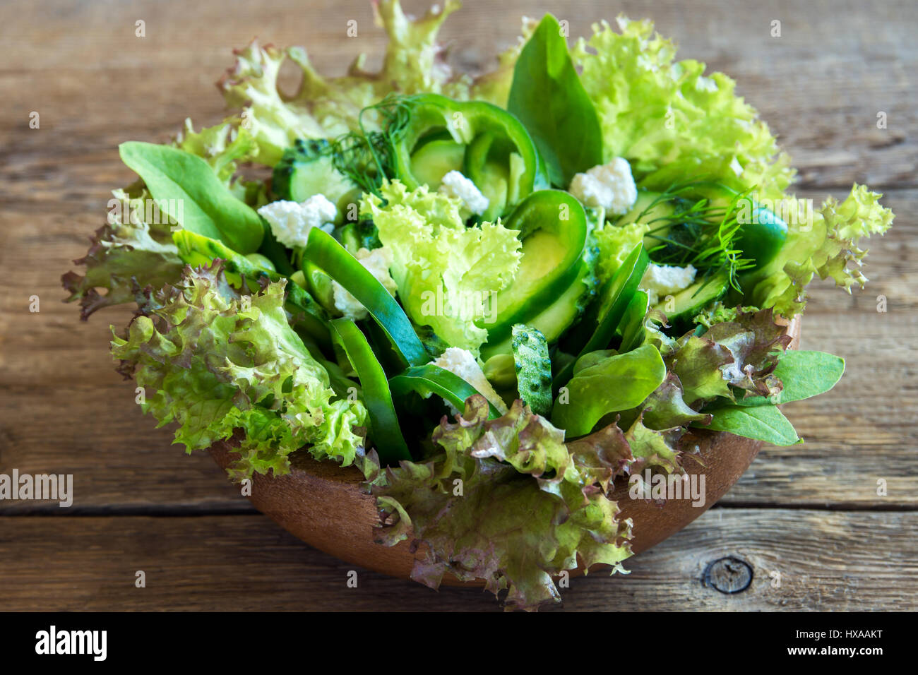 Organic mixed green vegetable salad with feta cheese and spring peas in wooden bowl close up - healthy diet organic vegan vegetarian food meal salad Stock Photo