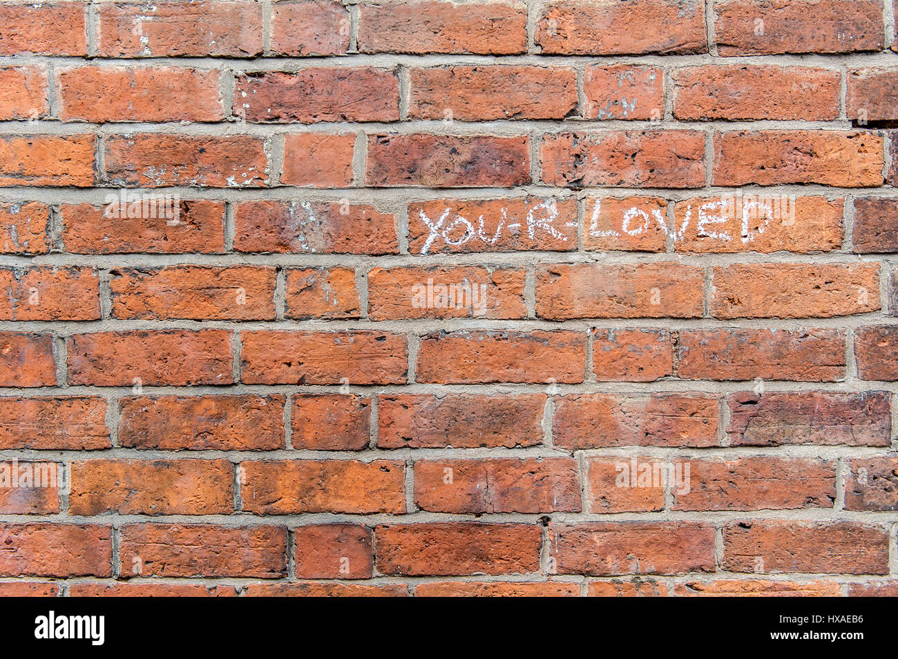 Red brick wall with the words you-r-loved written in chalk with copy space. Stock Photo