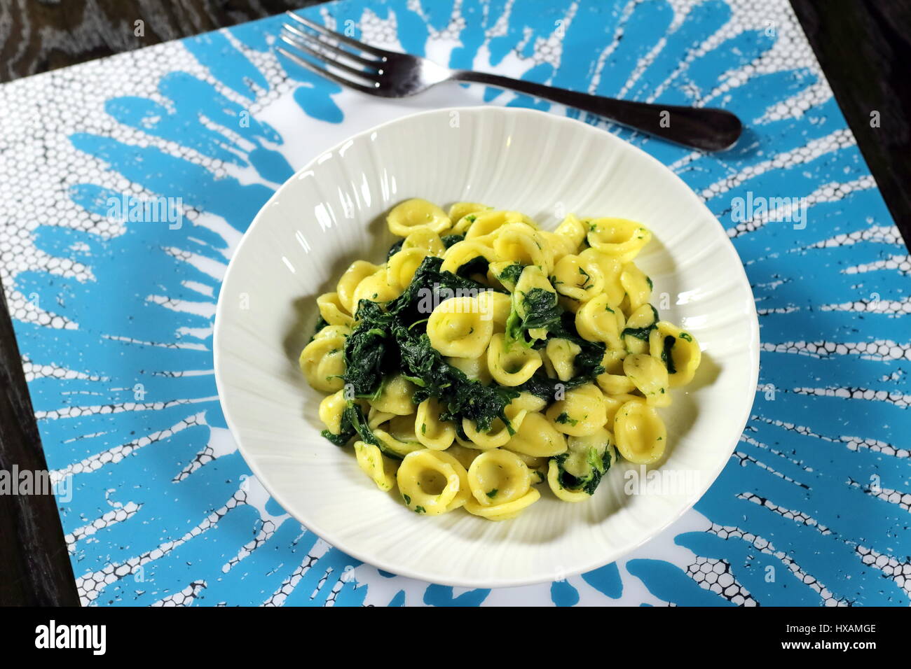 Turnip greens (collard greens) pasta (Italian Orecchiette alle cime di rapa) served in a white dish with fork on white and light blue placemat Stock Photo