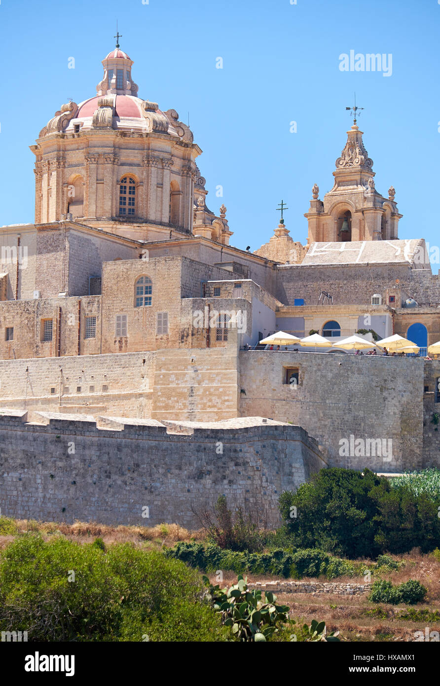 The view of the St. Paul's Cathedral in the old capital Mdina surrounding by the fortress wall from the countryside below. Malta Stock Photo