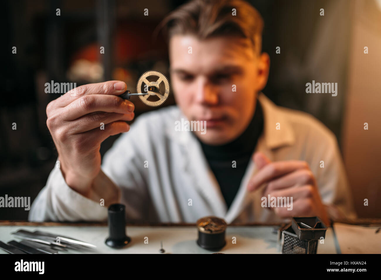 Watchmaker holding with tweezers a gear of old hours. Broken mechanical watches repairing Stock Photo