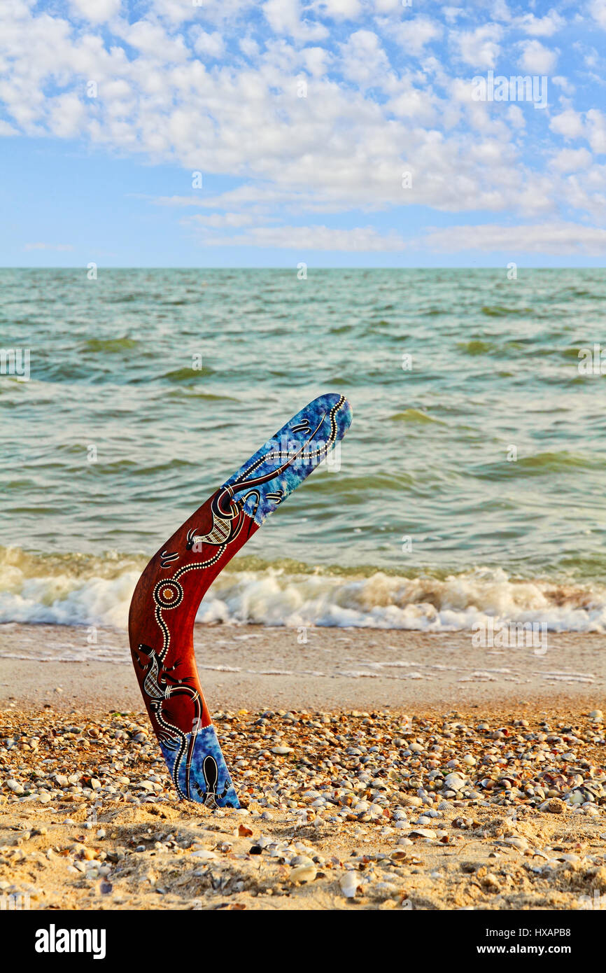 Australian Boomerang on sandy beach against of sea surf and cloudy sky