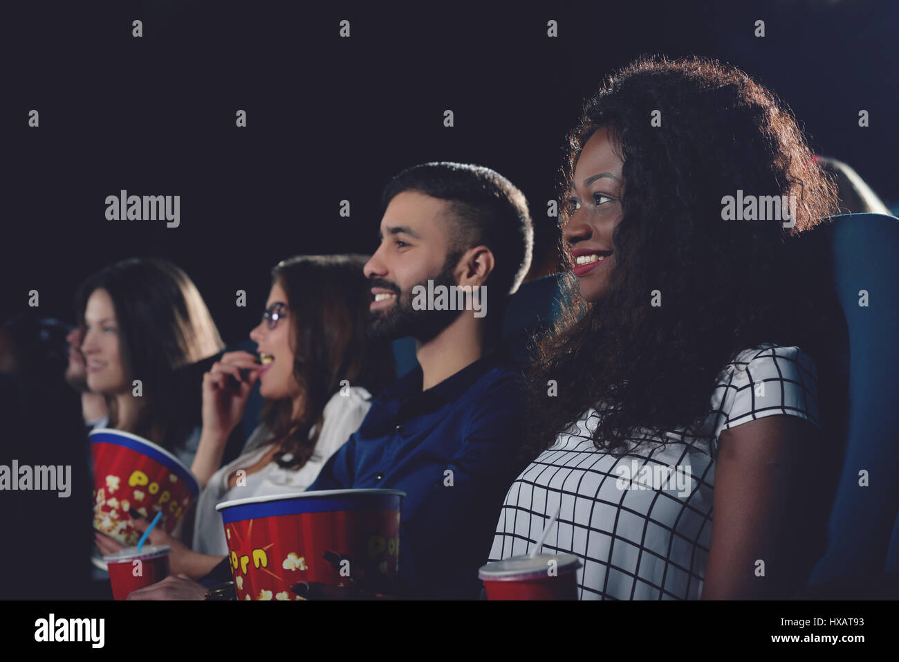 Curly african girl toothy smiling and watching film in cinema. Stock Photo