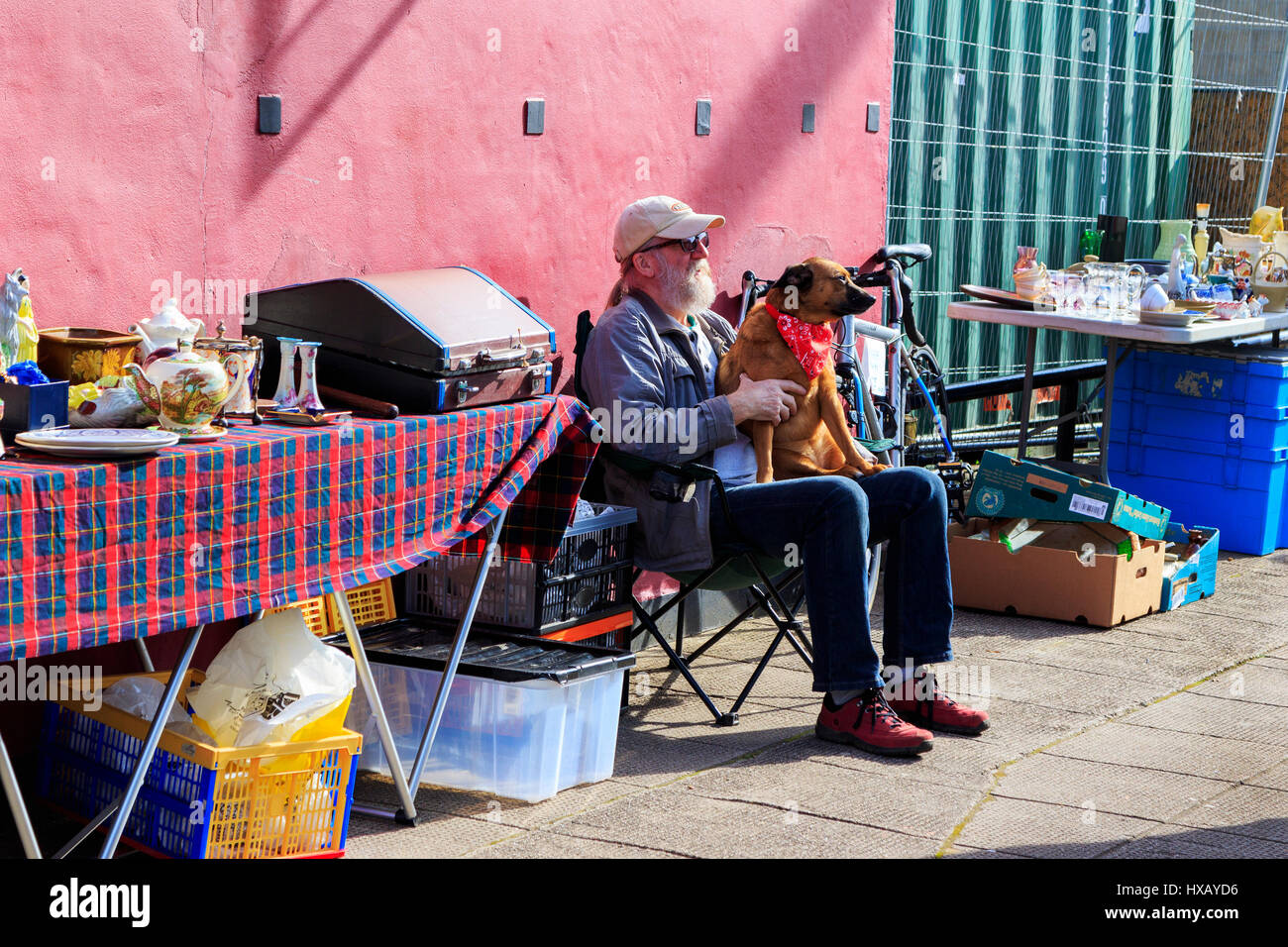 Stallholder at Glasgow's famous Barras open air and street market, sitting in the sun petting his dog. Glasgow. Scotland.UK Stock Photo
