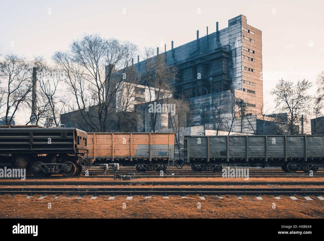 Railway station with freight wagons and train against metallurgical plant at sunset. Colorful industrial landscape. Railroad with vintage toning. Rail Stock Photo