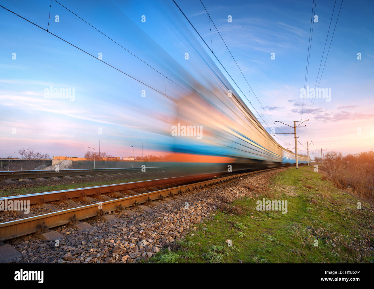 High speed passenger train in motion on railroad at sunset. Blurred commuter train. Railway station against colorful sky. Railroad travel, railway tou Stock Photo