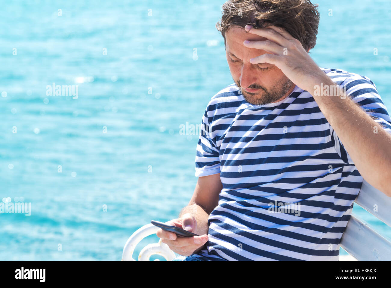 Male tourist in stripped shirt using mobile phone for communication at seaside on summer holiday vacation Stock Photo