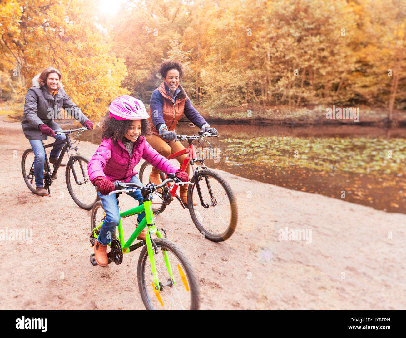 Young family bike riding along pond in woods Stock Photo