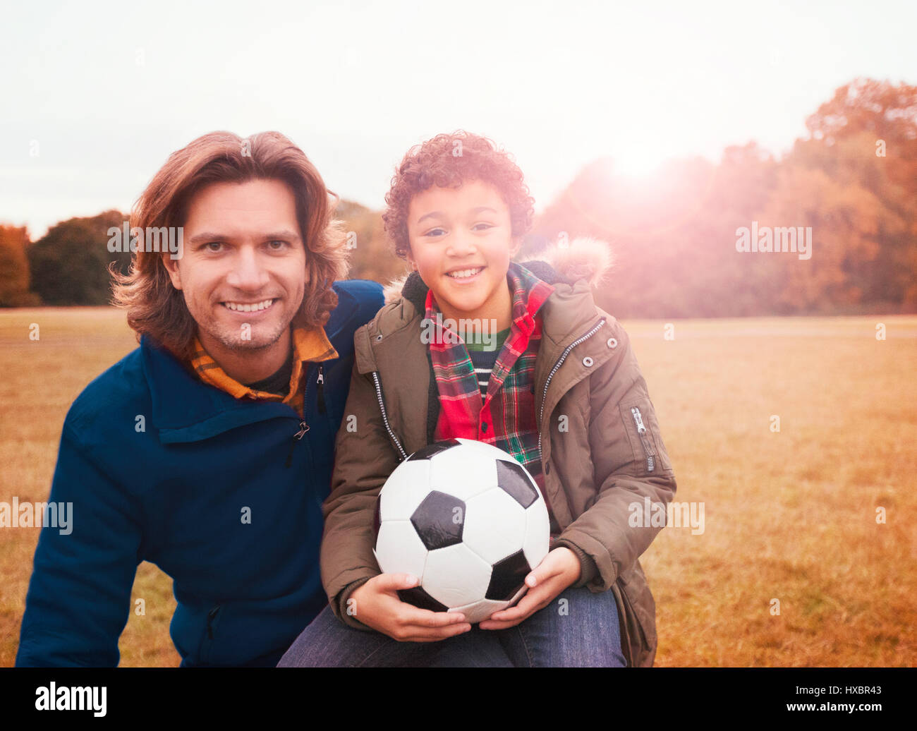 Portrait smiling father and son with soccer ball in park grass Stock Photo