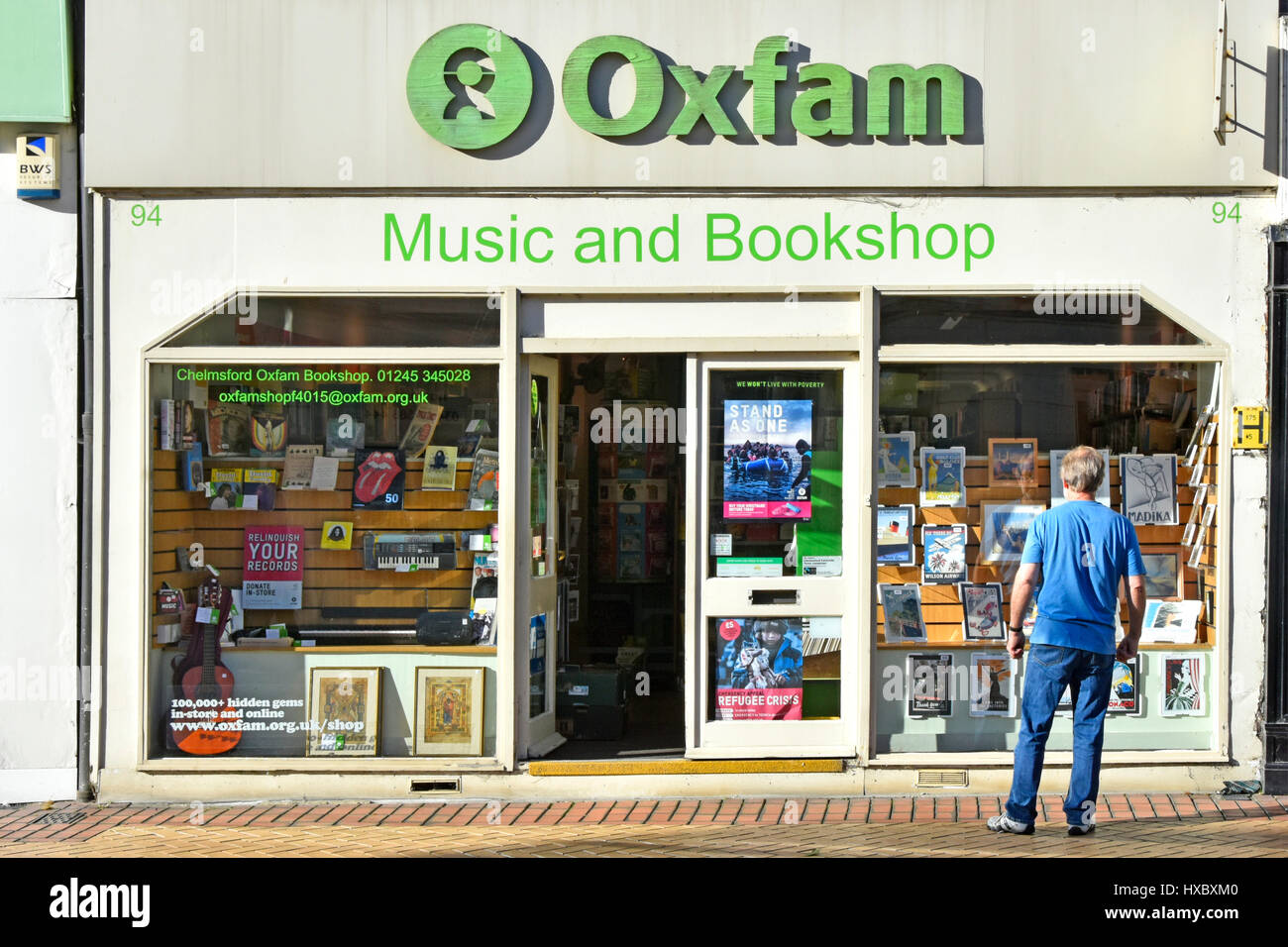 Town centre shopping street Oxfam charity music store & bookshop shop front with man window shopping Chelmsford High Street Essex England UK Stock Photo