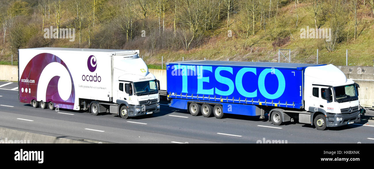 Ocado online supermarket distribution lorry overtaking Tesco supermarket store distribution truck on M25 UK motorway both with brand advertising Stock Photo