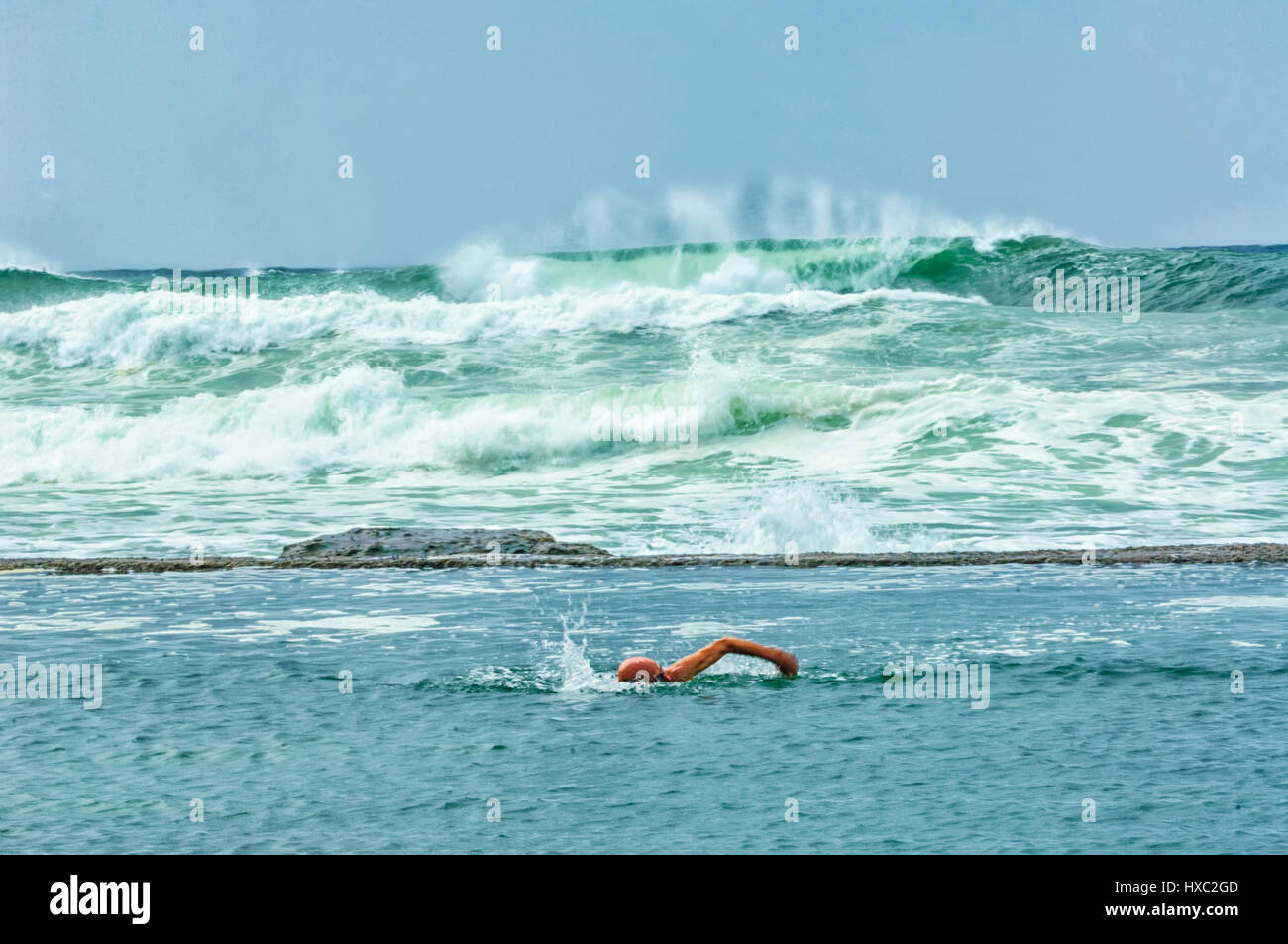 Man swimming in a rock pool in front of rough seas with large breaking waves, Gerringong, Illawarra Coast, New South Wales, NSW, Australia Stock Photo