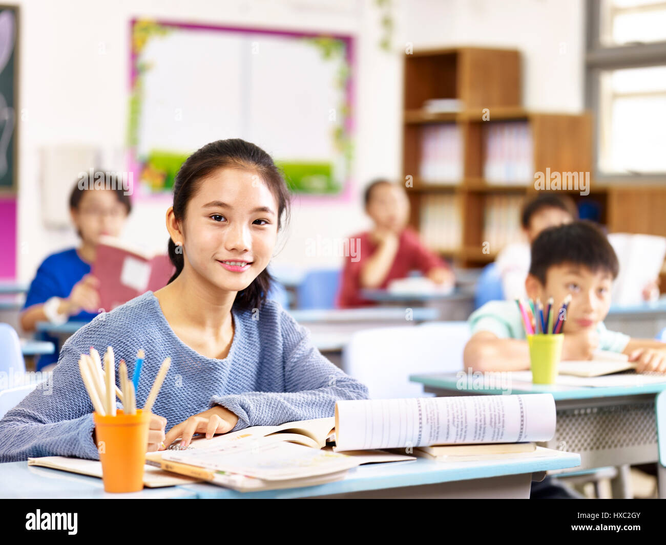 portrait of asian elementary schoolgirl sitting in classroom with classmates. Stock Photo