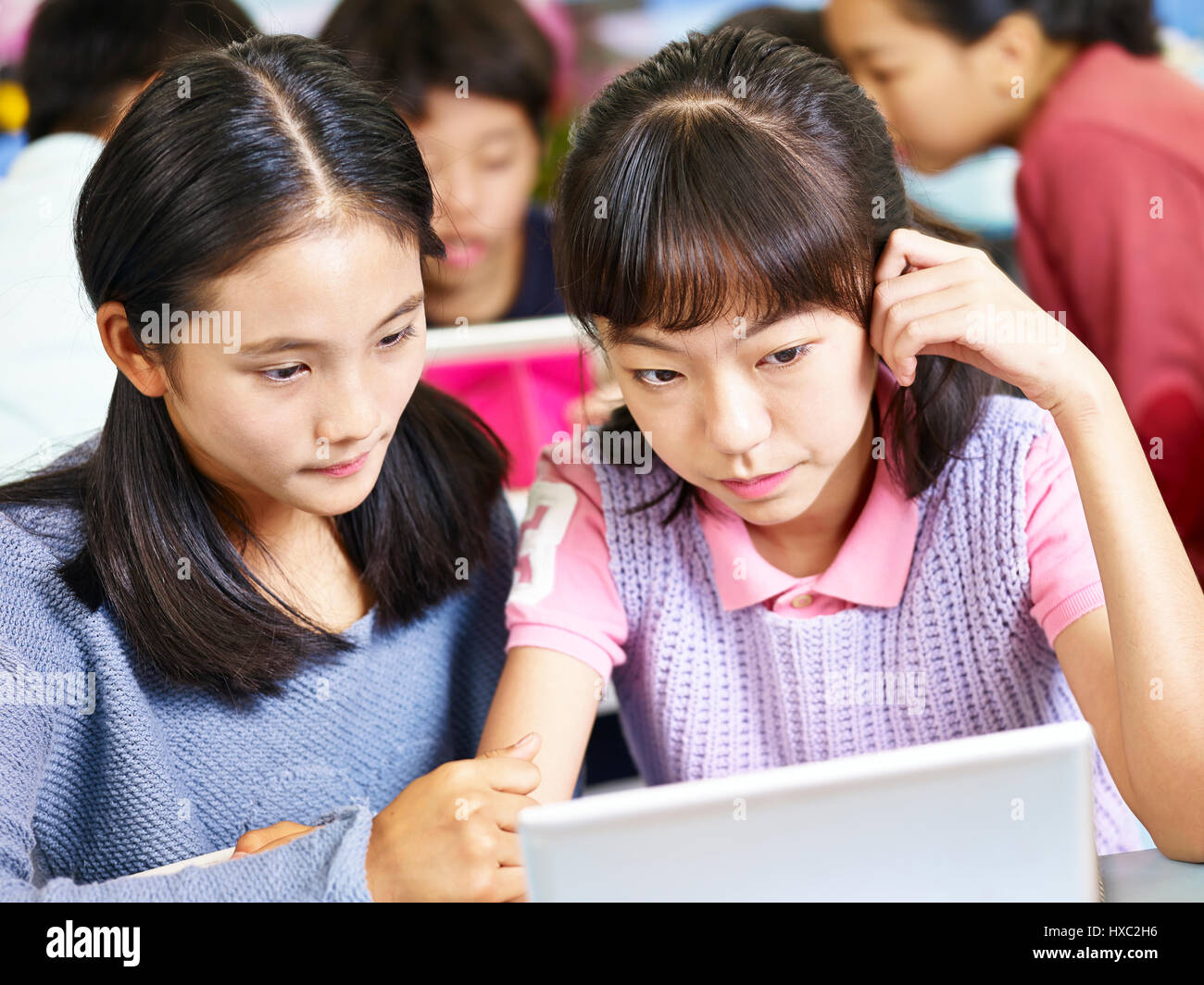 two asian elementary school girls looking at tablet computer thinking hard while working in groups. Stock Photo