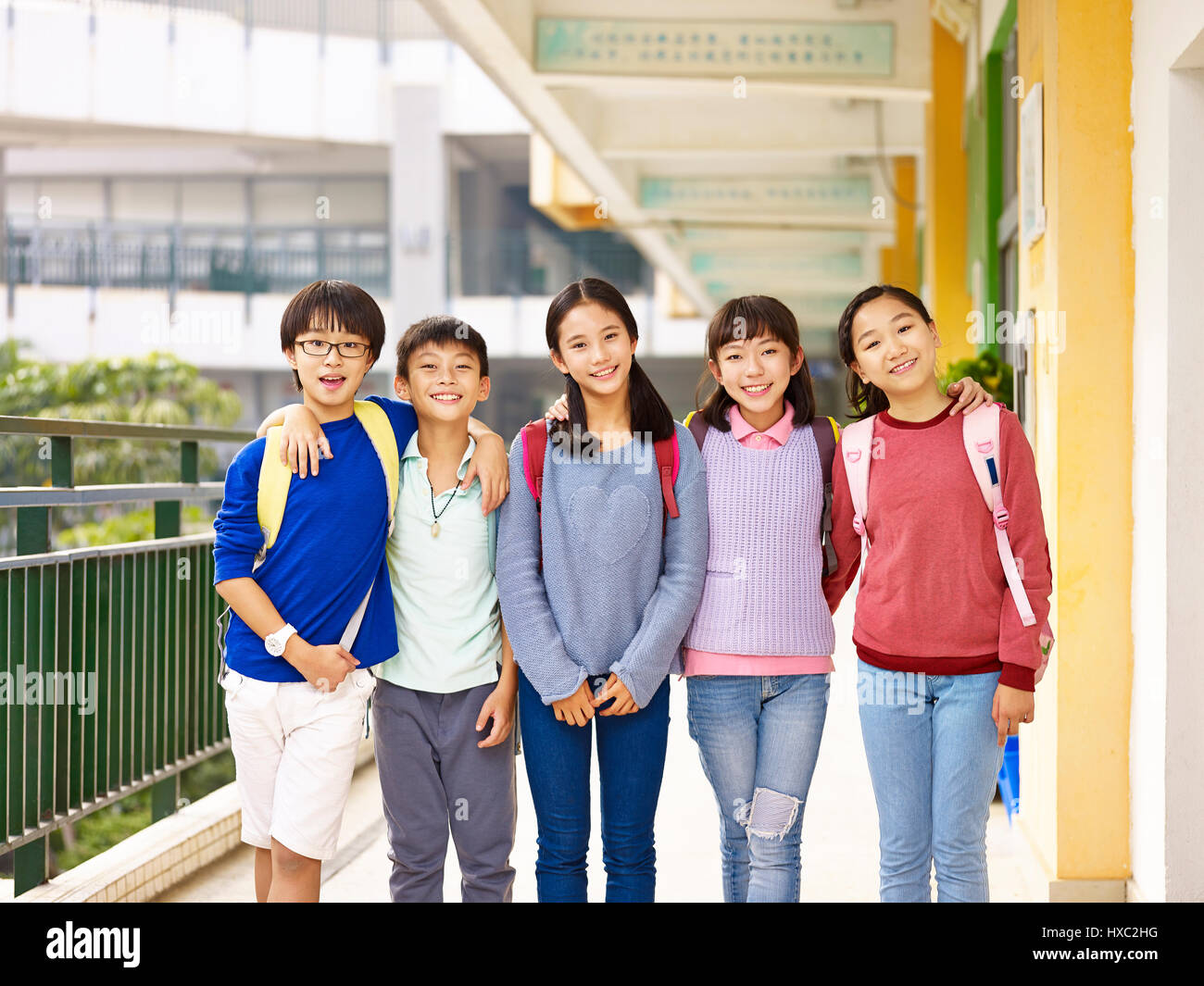 group of happy and smiling elementary schoolboys and schoolgirls standing in hallway of classroom building on campus. Stock Photo