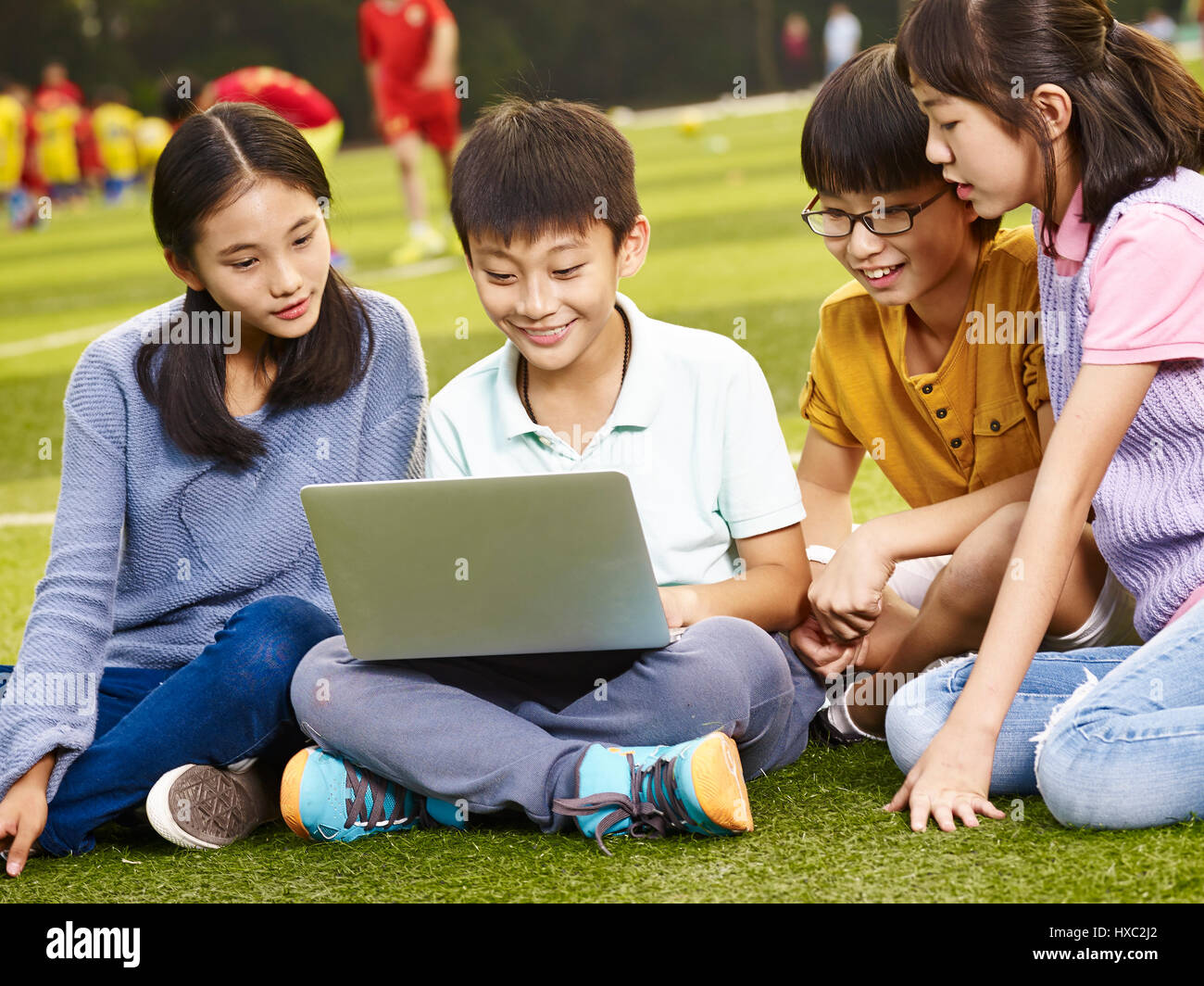 four asian elementary school children using laptop computer outdoors. Stock Photo