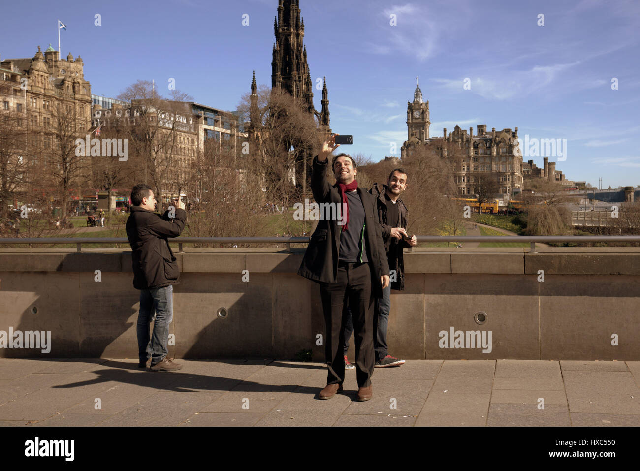 Tourists in princes street gardens at the National Museum of Scotland take selfies selfie selfy selfie with Edinburgh panorama as a backdrop Stock Photo