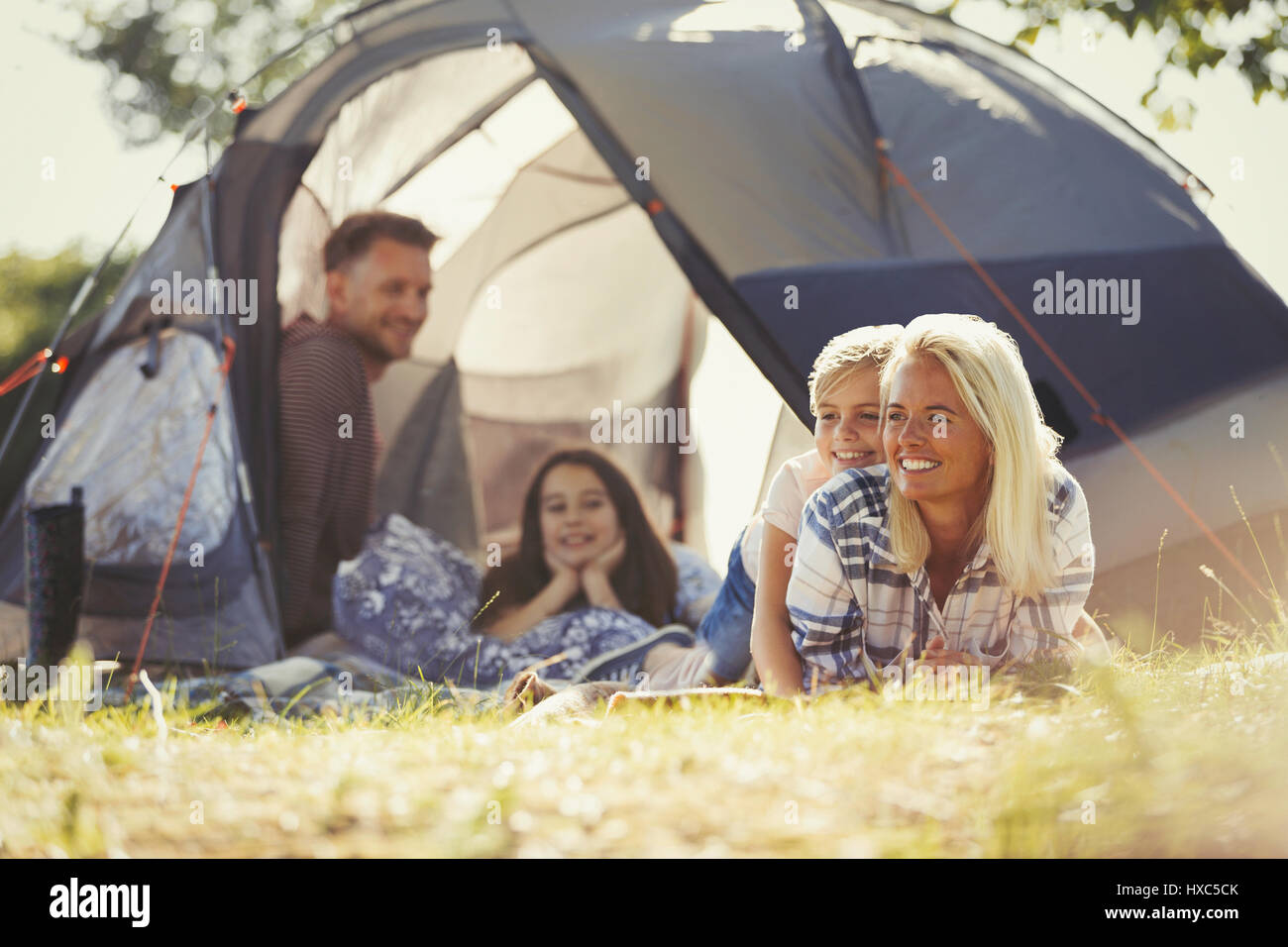 Smiling family relaxing outside sunny tent at campsite Stock Photo