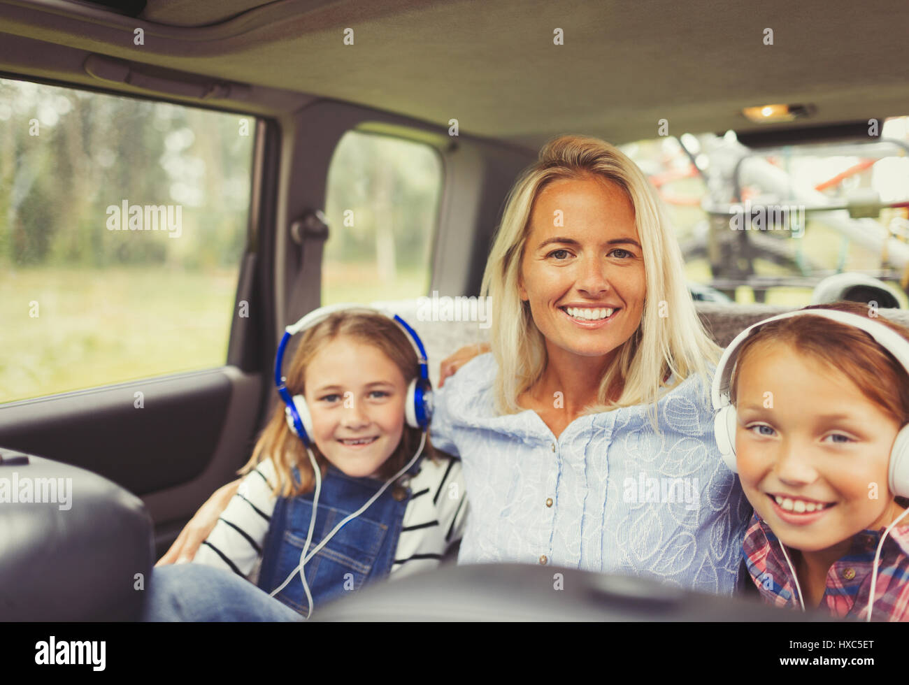 Portrait smiling mother and daughters wearing headphones in back seat of car Stock Photo